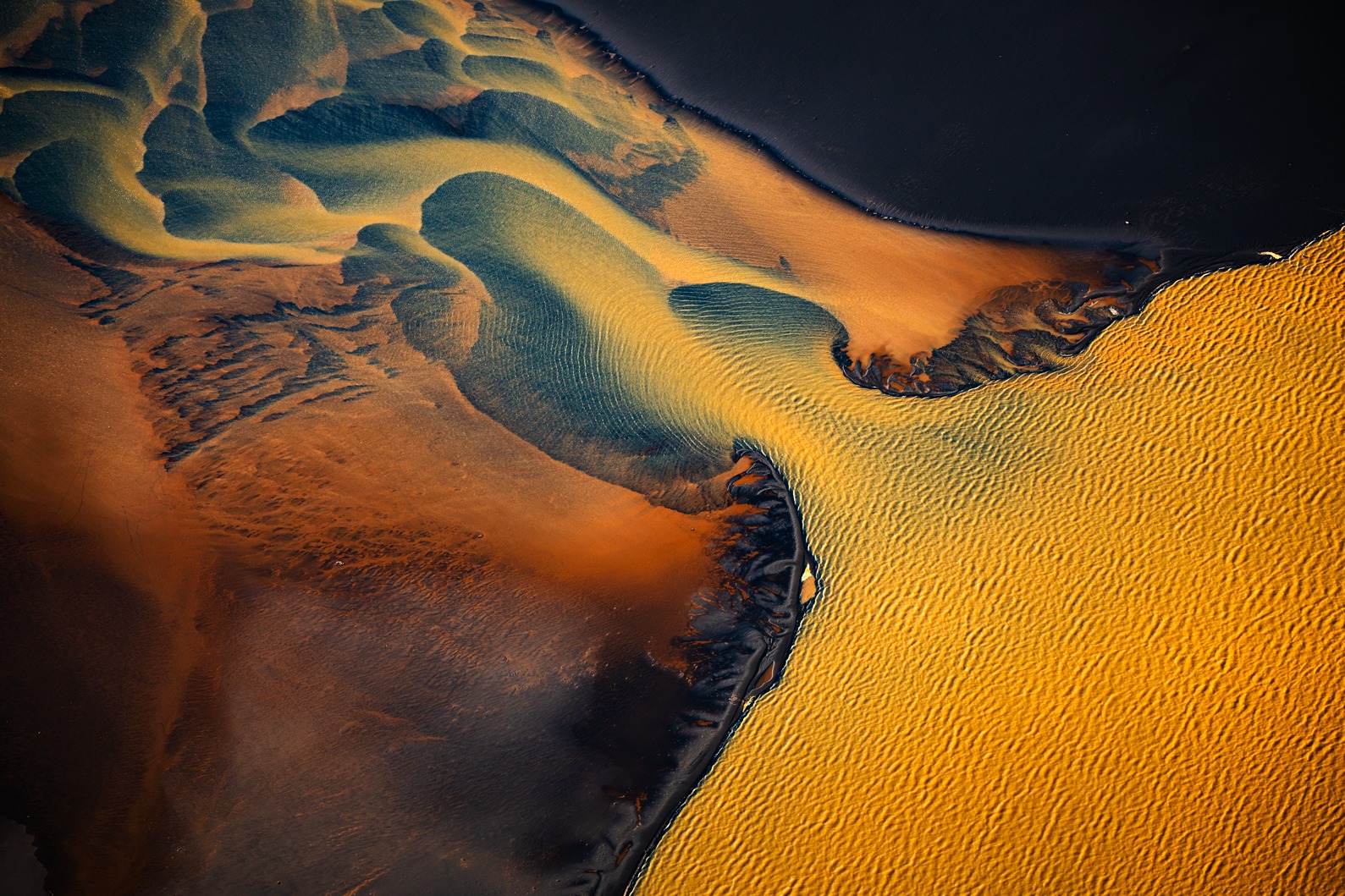 Aerial view of natural basin formations with golden sand meeting dark water